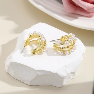 Close-up of elegant C-shaped gold hoop earrings with small white pearls on stone