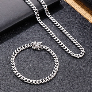 Close-up of silver Cuban chain necklace and bracelet set with embossed box clasp on black texture