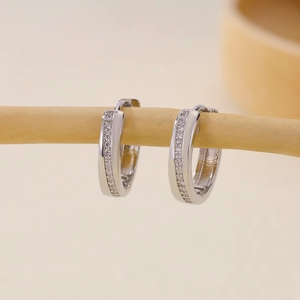 Pendientes de aro plateados con circonitas blancas brillantes en un soporte de madera