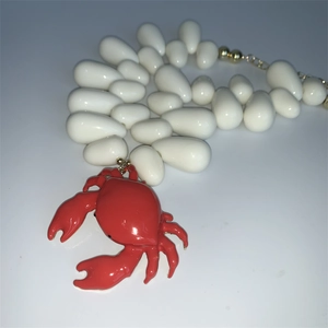 Detail of red crab pendant on a white teardrop beaded choker necklace with gold clasp