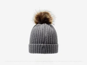 Close-up of gray knit beanie featuring a brown faux fur pom and ribbed texture