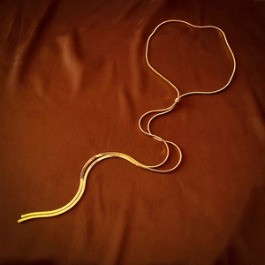 Close-up of golden snake bone chain necklace with sliding adjustment on silk fabric