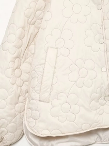 Detail of floral quilted pattern and matching snap buttons on white cotton jacket