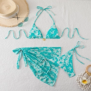 Flat lay of a three-piece floral bikini set with halter top and matching sarong scarf