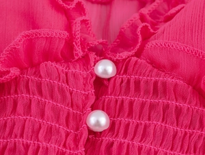 Détail d'une robe en mousseline rose avec texture smockée, volants et boutons perles
