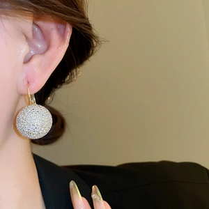 Close-up of a sparkling gold spherical earring with inlaid rhinestones on a female model