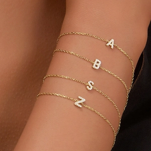 Close-up of four gold bracelets with zircon-inlaid A, B, S, N letter charms on a wrist