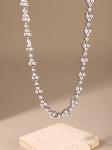 Detailed view of stainless steel necklace with white pearls on a beige stone base