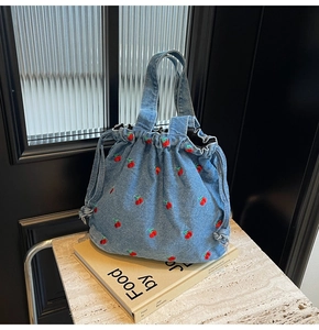 Detail of blue denim bucket bag featuring vibrant red cherry embroidery and drawstring closure