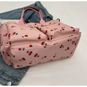 Detail view of pink tote bag with red cherry prints and silver metal zippers