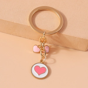 Detail of a gold metal keychain featuring pink enamel bow and white heart round charms