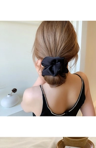Detail of a large black satin scrunchie showing soft pleats and glossy fabric texture