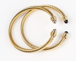 Detail of twisted cable cuff bracelets in gold with black and silver spherical ends