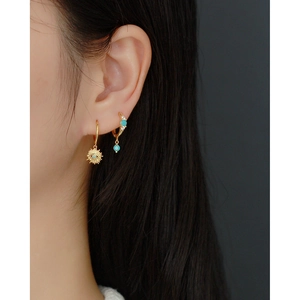 Detail of S925 silver gold hoop earrings with turquoise and sun charm on ear