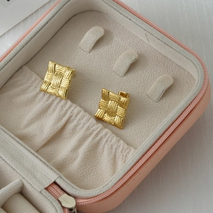 Detail of square gold stud earring with woven texture in a pink leather jewelry box