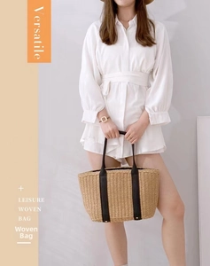 Detail of hand-woven straw tote bag with black leather handles held by a model