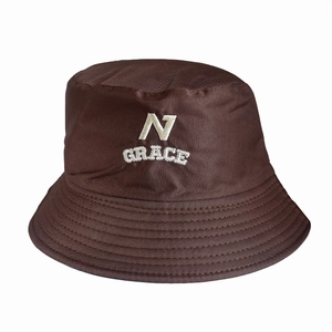 Detail of dark brown bucket hat featuring white embroidered N GRACE logo on canvas