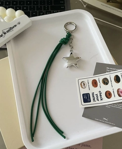 Detail of silver star keychain with dark green braided rope on a minimalist white tray