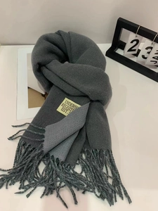 Detail of color-block scarf with fringes and logo label on white surface