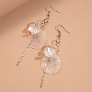 Detail of beaded shell earrings with silver flowers and tassels on beige background