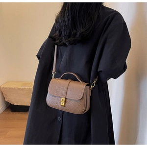 Detailed close-up of brown litchi grain leather bag with gold metal twist lock and handle