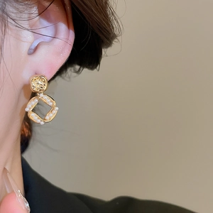 Detail of 18K gold-plated square pendant earrings with inlaid pearls on a model