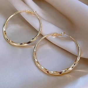 Detailed view of large gold twisted hoop earrings on champagne silk fabric background