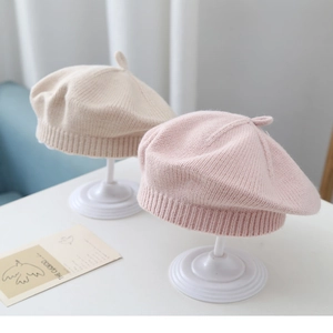 Detail view of soft knitted baby berets in beige and pink with cute decorative top knots