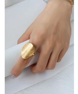 Close-up of golden irregular oval ring with a brushed matte texture on female finger