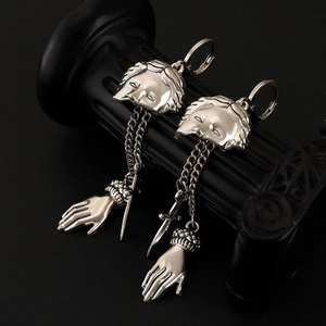 Detail of gothic silver earrings with masks, chains, and swords on a black column
