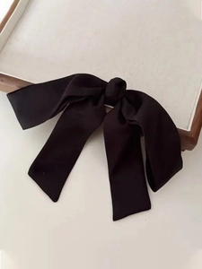 Close-up of a large black satin bow hair clip on a minimalist cream jewelry tray