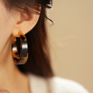 Close-up of model wearing large tortoiseshell resin C-shaped hoop earrings in amber brown