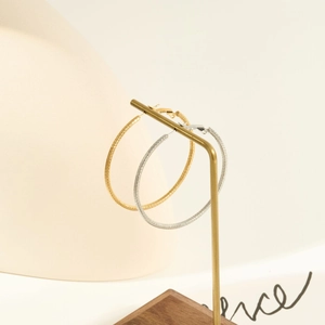 Detailed view of large textured hoop earrings in gold and silver on a minimalist display