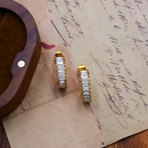 Detailed shot of golden C-shaped hoop earrings with rectangular zircon on vintage props