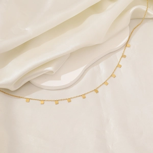Close-up of golden square pendant necklace on white silk fabric with elegant metal luster