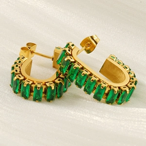 Detail of gold U-shaped earrings featuring emerald green rectangular gemstones on silk