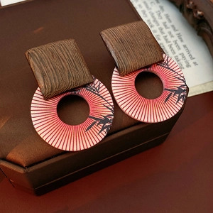 Macro shot of geometric earrings featuring wooden texture and bamboo silhouette on red pattern