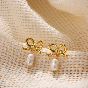 Elegant 18K gold bow earrings with dual baroque pearls on soft beige fabric background