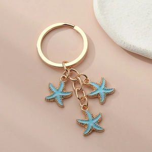 Close-up of golden keychain featuring three light blue enamel starfish charms on a pink surface