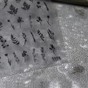 Close-up of black floral nail art stickers with delicate leaf patterns on gray background