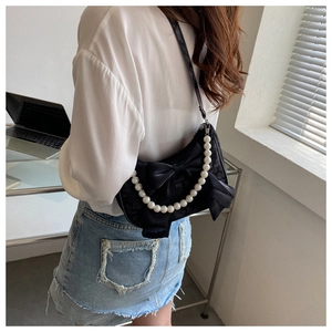 Detail of a black satin shoulder bag with a large bow and decorative oversized pearl strap
