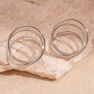 Detailed macro view of silver triple-layered twist rings on beige stone background