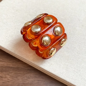 Detail of amber acrylic modular band with gold dome metal accents on book surface
