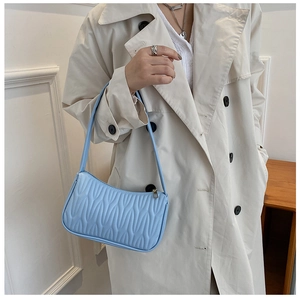 Detail of light blue underarm bag with wavy quilted texture and smooth PU leather finish