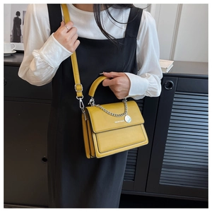 Detail of yellow crossbody bag featuring a golden chain strap and round fashion tag