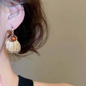Macro shot of gold fan-shaped earrings with champagne crystals and brushed metal texture