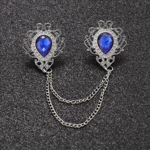 Close-up of vintage silver brooches with blue teardrop gems and double metal chains
