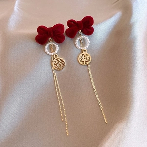 Détails de boucles d'oreilles festives avec nœuds rouges et longs pompons dorés élégants