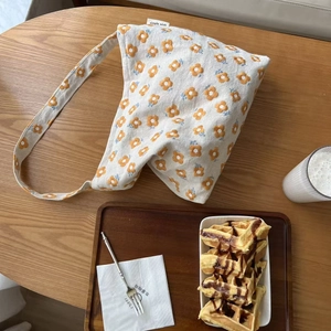 Canvas shoulder bag with yellow flower embroidery and simple wish label on a wooden table