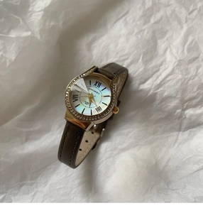 Close-up of a women's gold oval watch with rhinestone bezel and grey leather strap